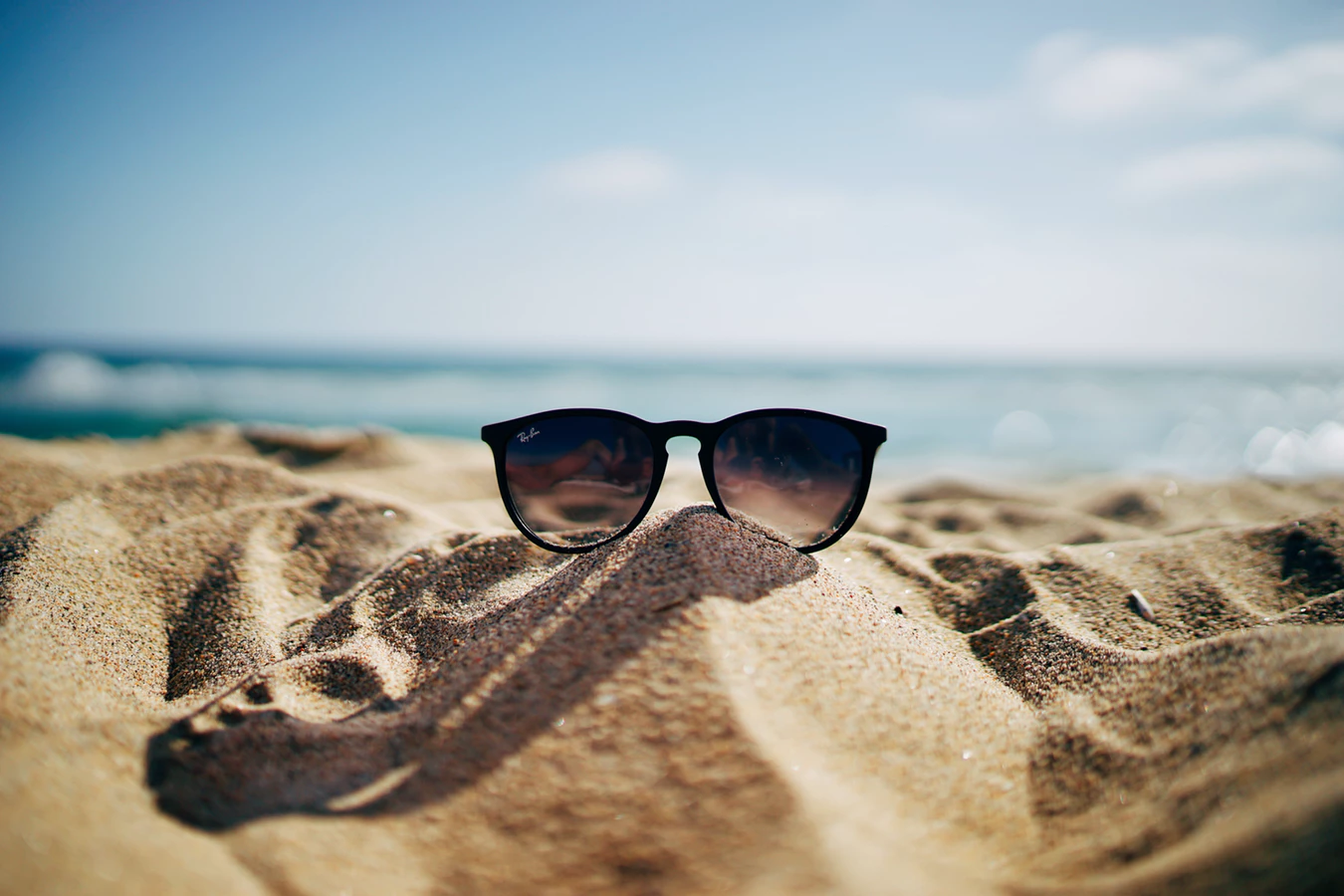 Sunglasses in the sand with the ocean in the background