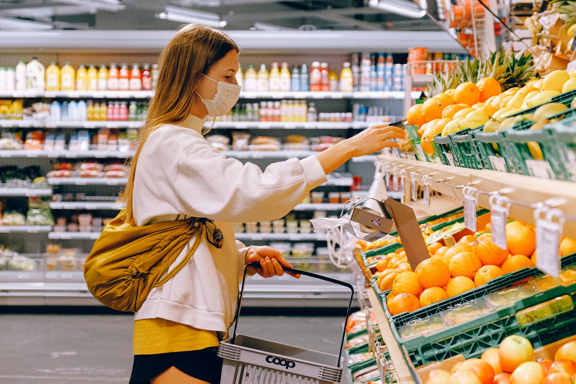 woman picking out fruit at a grocery store wearing a mask