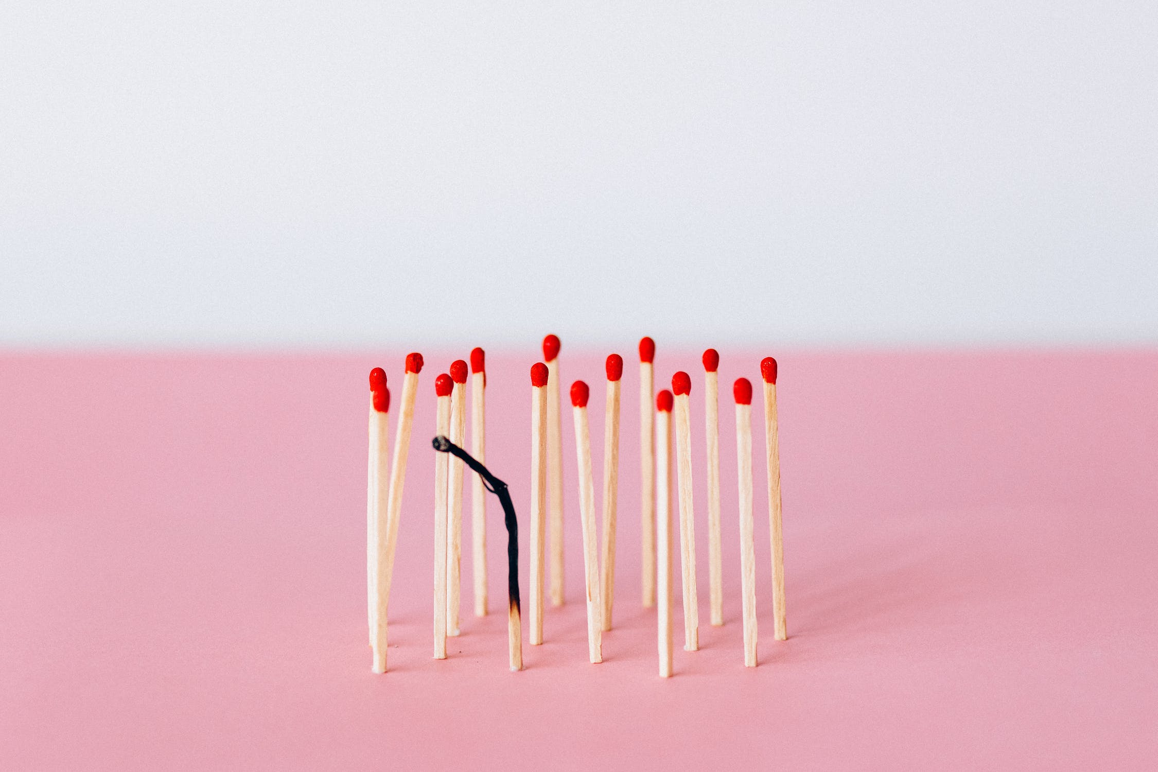 a group of matches with one burnt out against a pink background