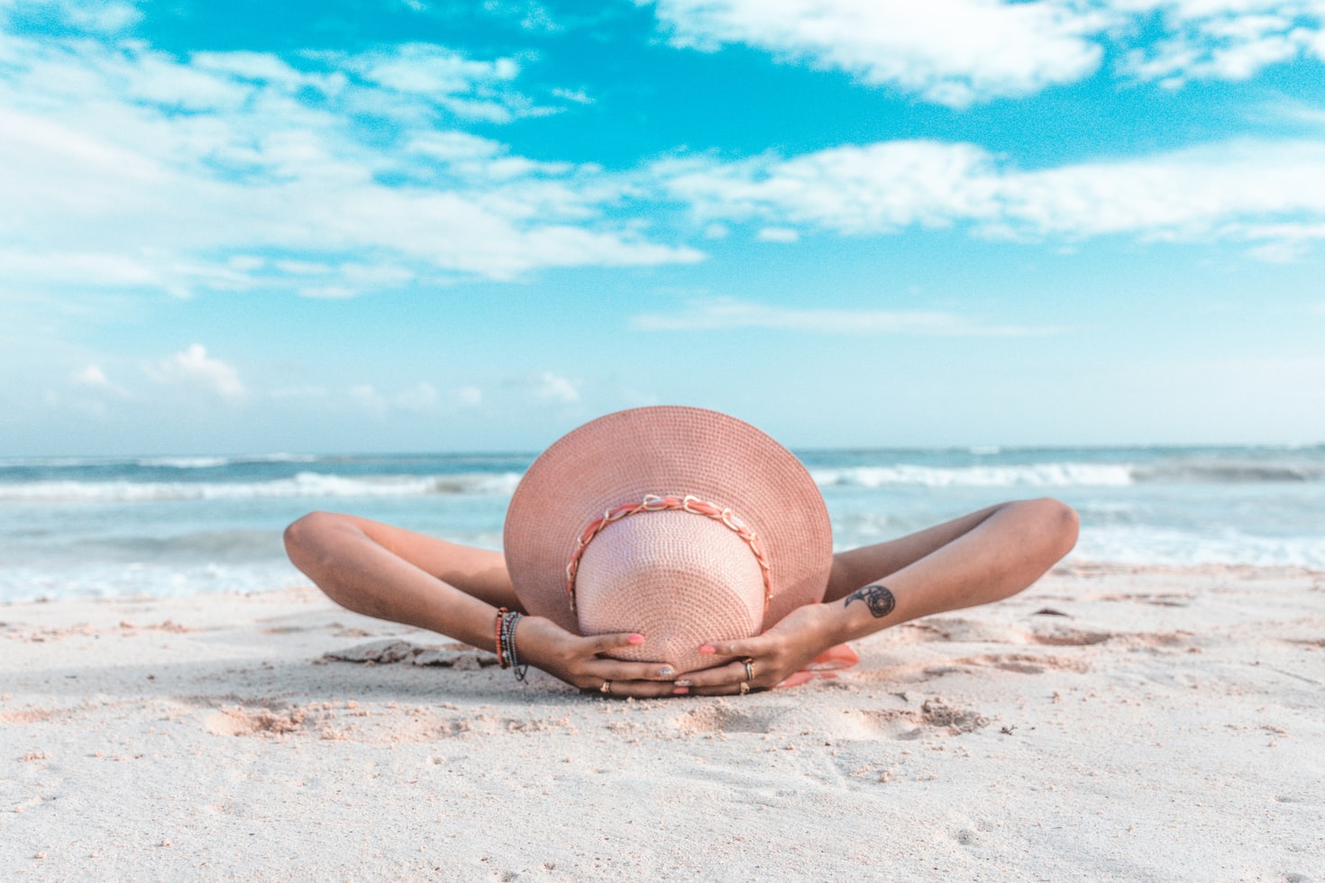 woman in sunhat laying on beach with blue skies behind her