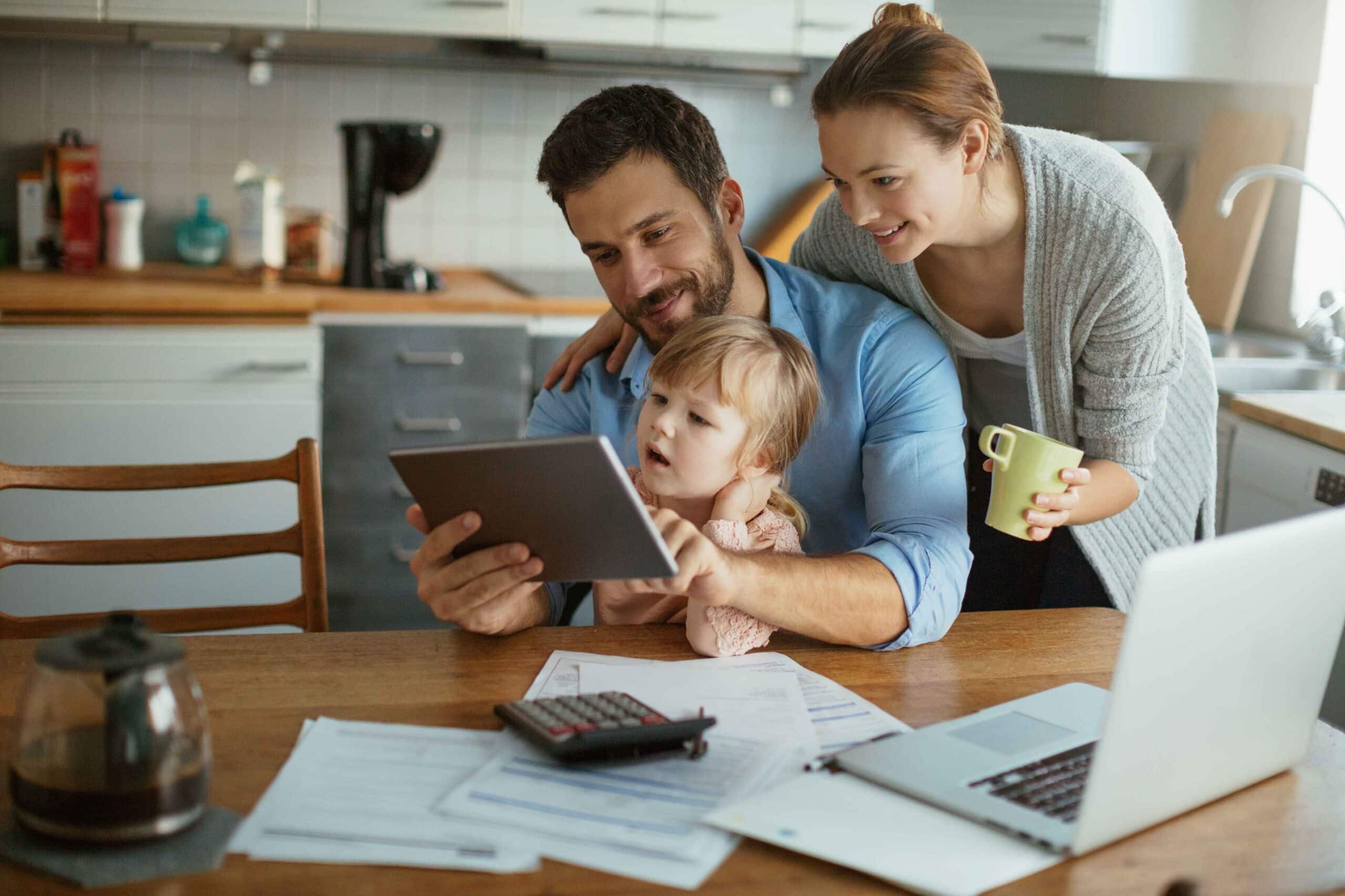 smiling family of three using tablet to manage financials together at kitchen table