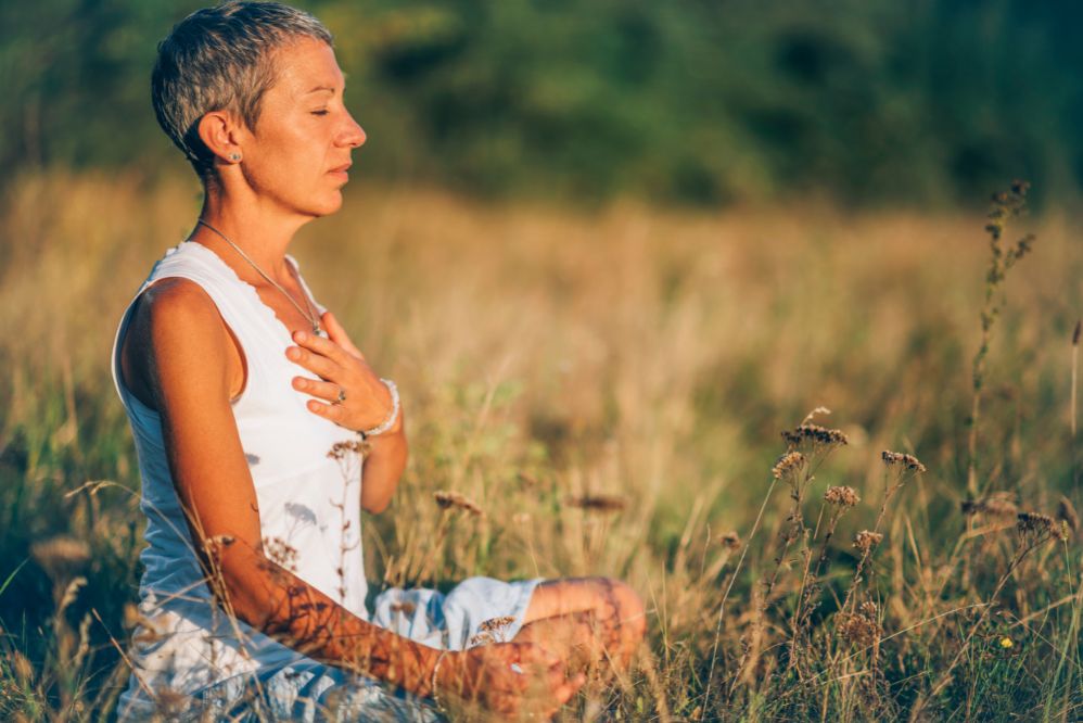 Woman in a field, holding her chest, eyes closed, meditating
